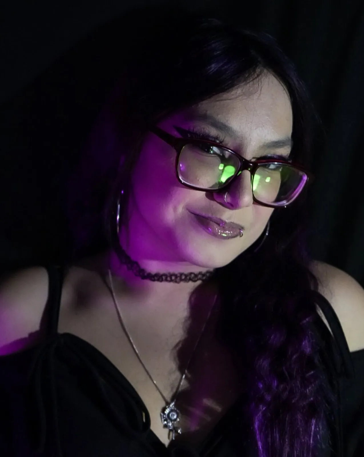A young woman in glasses lit by deep violet light against black