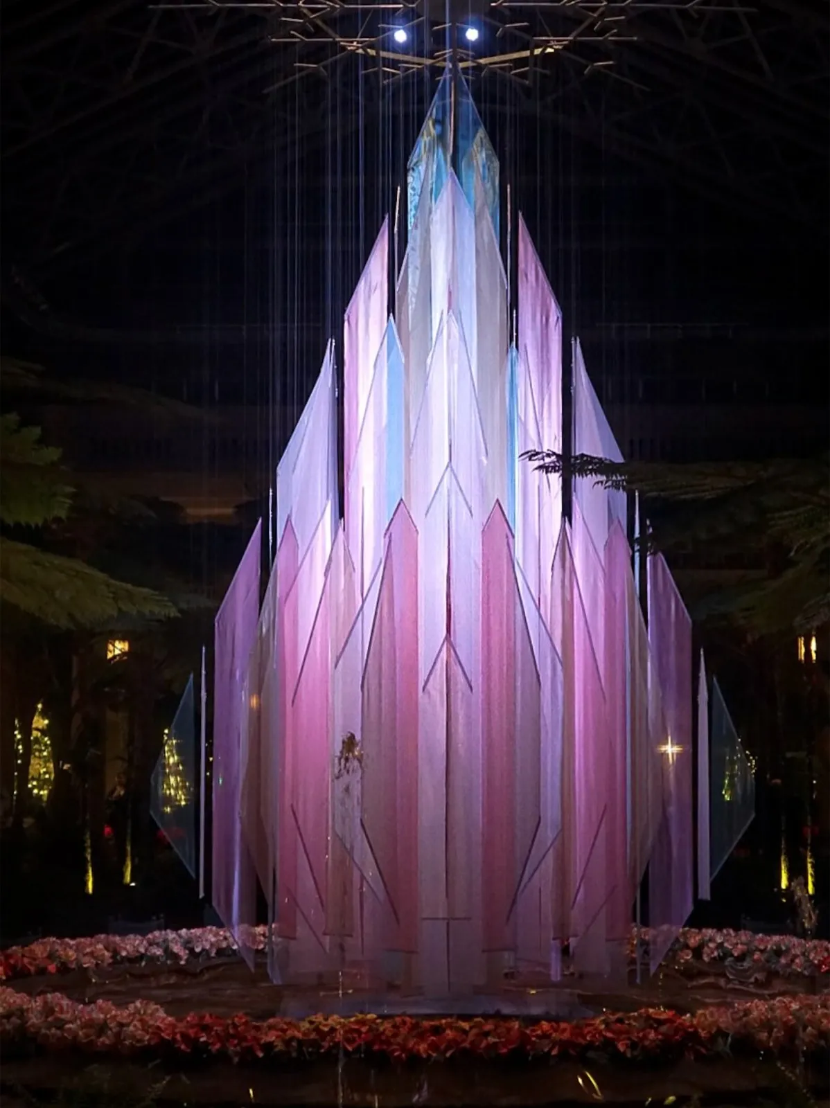 A towering crystalline spire sculpture lit in pink and blue in a darkened atrium