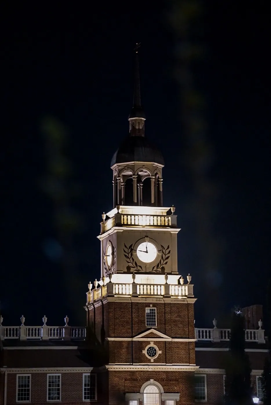 A floodlit brick clock tower with a domed steeple against a black night sky