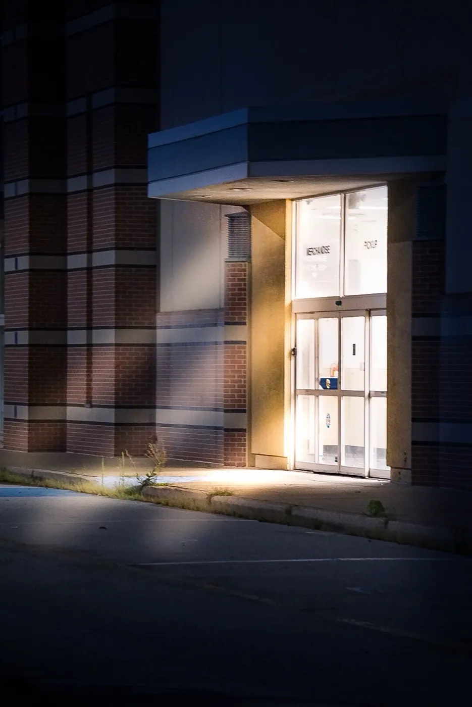 A glowing lit doorway of a darkened building at night, light spilling onto the pavement